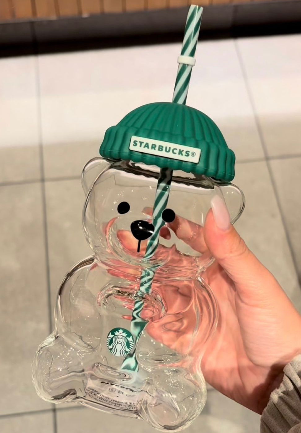 Starbucks bear-shaped glass with green lid and straw held by a hand.