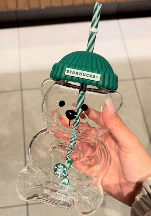 Starbucks bear-shaped glass with green lid and straw held by a hand.